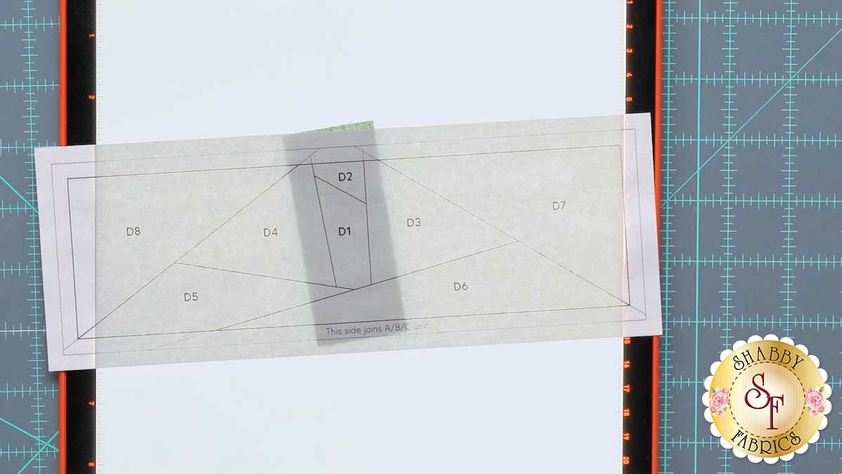 fpp_series_4_june_paper_on_piece.jpg A foundation paper on a lit light pad, showing the first fabric piece covering its shape with a quarter inch margin.