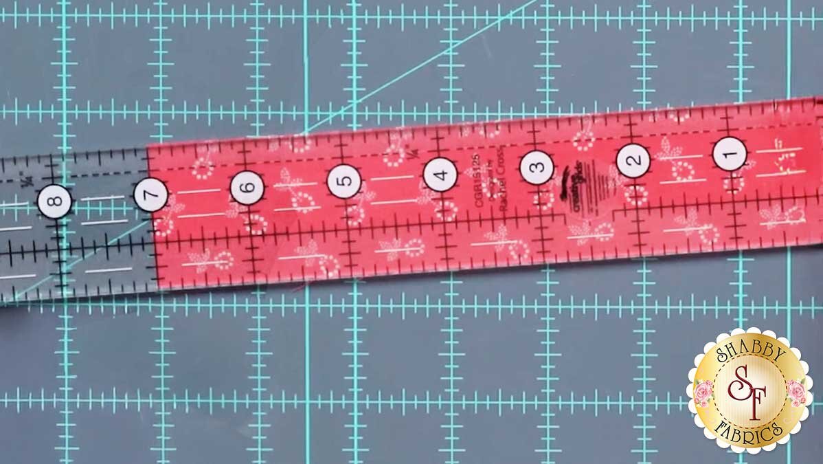 sew_cute_june_7_inches.jpg A 1.5 by 12.5 inch ruler laid along a fabric strip, positioned to cut a log to an exact length.