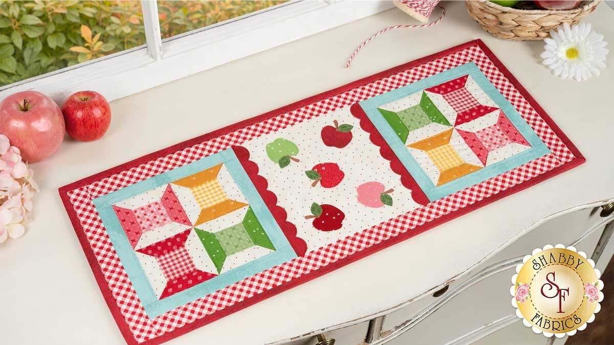 sew_cute_runner_september_pro_pic.jpg A quilted table runner with applique apples and thread spool shapes.