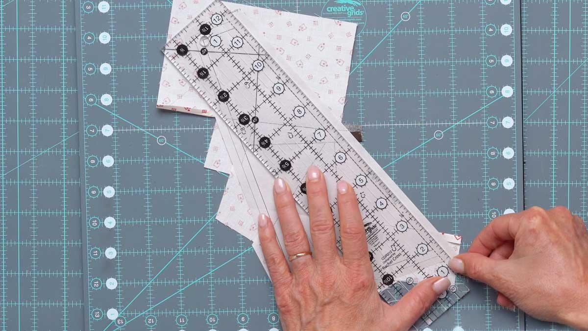 fpp_september_1200x675_using_cg_ruler_for_cut.jpg A ruler placed along the outermost printed line of a finished foundation section, ready to trim away the excess fabric.