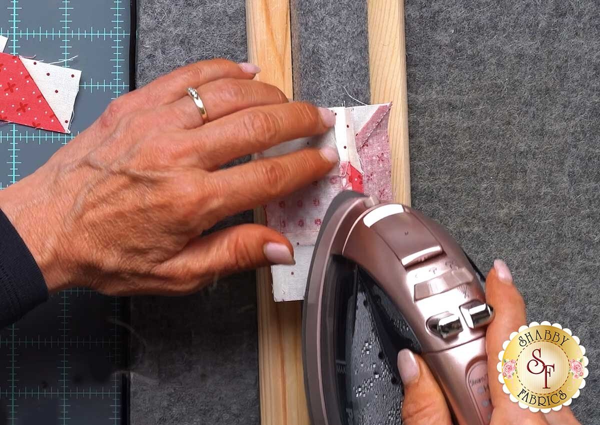 sew_cute_runner_september_presser_bar_pressing.jpg A wooden clapper resting on a freshly pressed seam on a wool pressing mat.